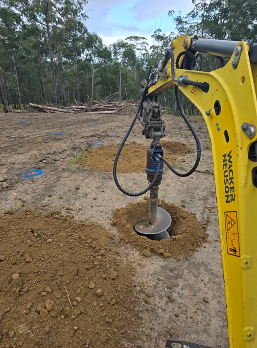 Post hole auger boring holes on a cleared site