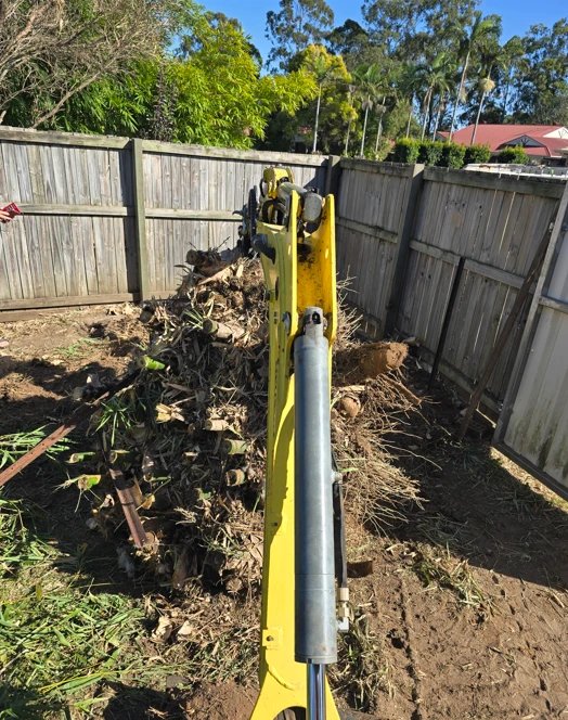 Excavator clearing palm stumps and debris from a residential yard